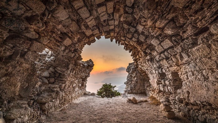 Ruins of an ancient stone archway overlooking a sunset sea landscape