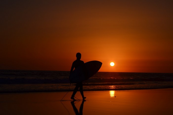 Surfer walking on beach at sunset