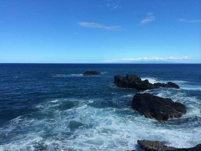 Ocean waves crashing on dark rocks near the horizon