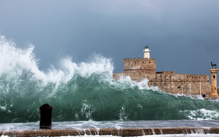 Waves crashing against a stone fort with a lighthouse