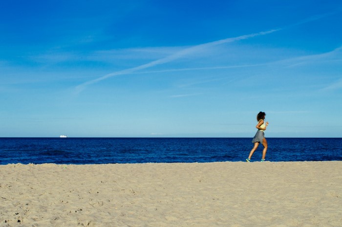 Woman running on a beach with the ocean and sky