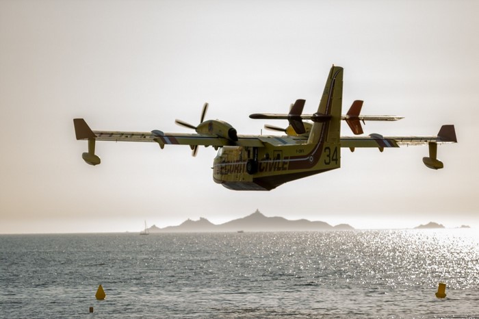 Yellow Canadair CL-415 water bomber aircraft flying over the sea