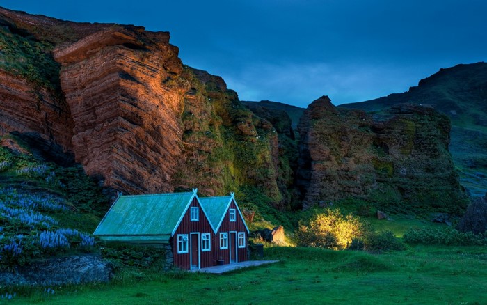 Two red houses with green roofs at the base of a cliff