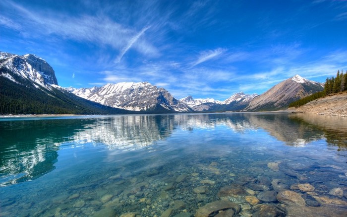 Snowy mountains reflected in a clear lake under a blue sky