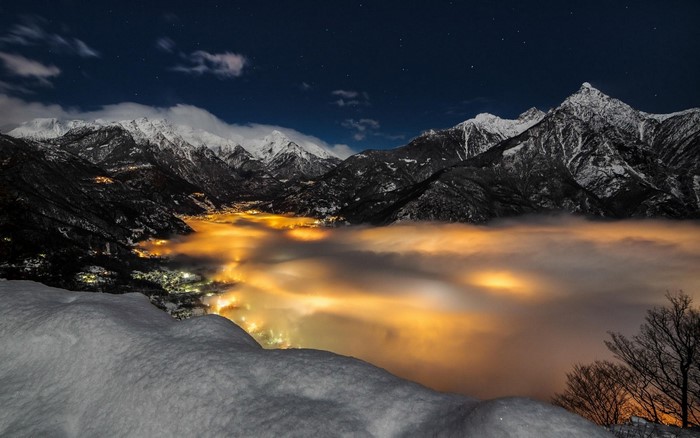 Snowy mountains over a valley with fog and city lights at night