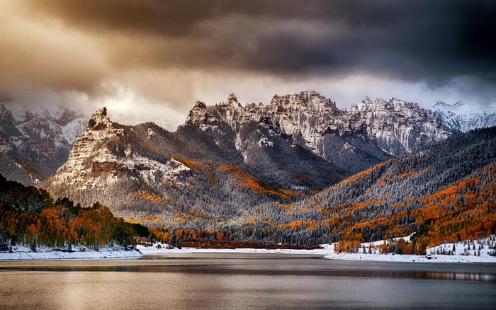 Snow-dusted mountains and autumn forest by a lake
