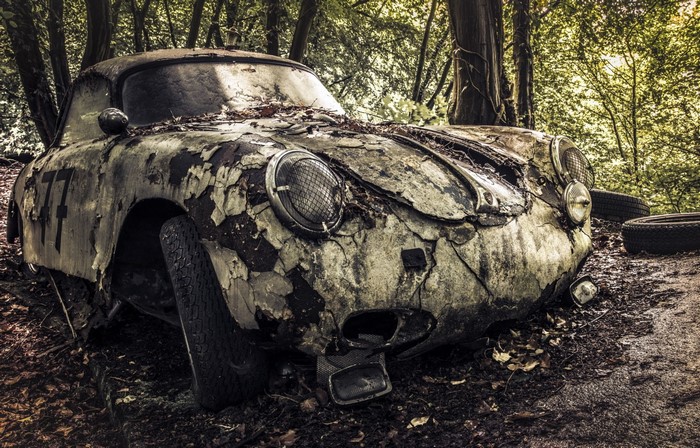 Abandoned vintage sports car with number 77 in a forest