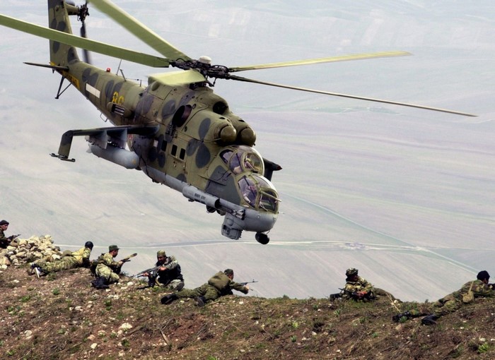 Mil Mi-24 Hind helicopter flies over soldiers on a hill