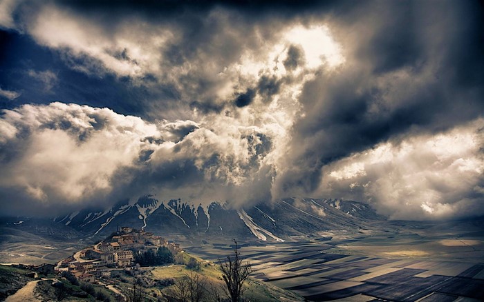 Village on a hill under stormy clouds and snowy mountains
