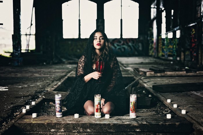 Woman in black lace veil holding red glass with candles