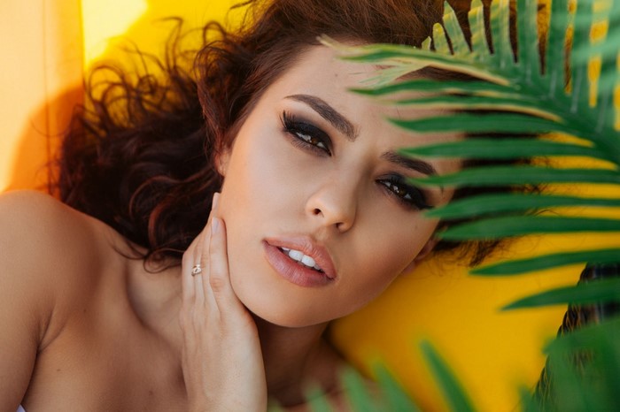 Woman with dark hair and makeup, partially hidden by leaves