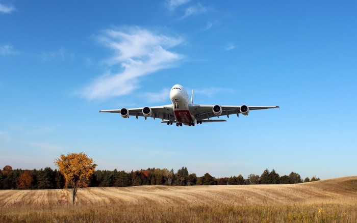 Airbus A380 passenger jet flying over a rural landscape