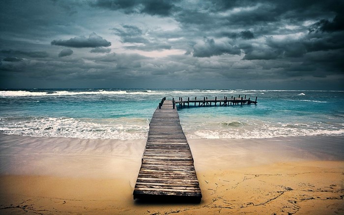 Wooden pier extending into the ocean under stormy clouds