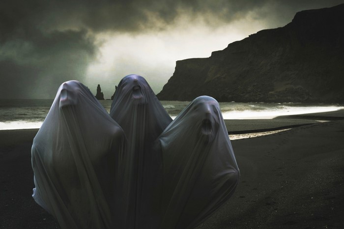 Three ghosts on a dark beach with sea stacks