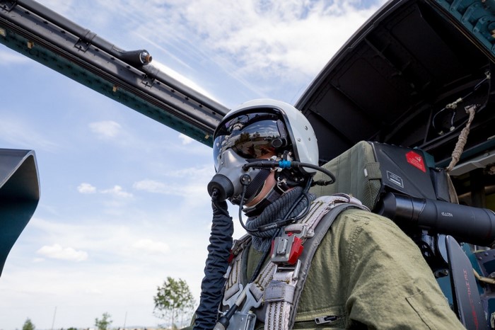 Pilot in a fighter jet cockpit wearing a helmet and oxygen mask