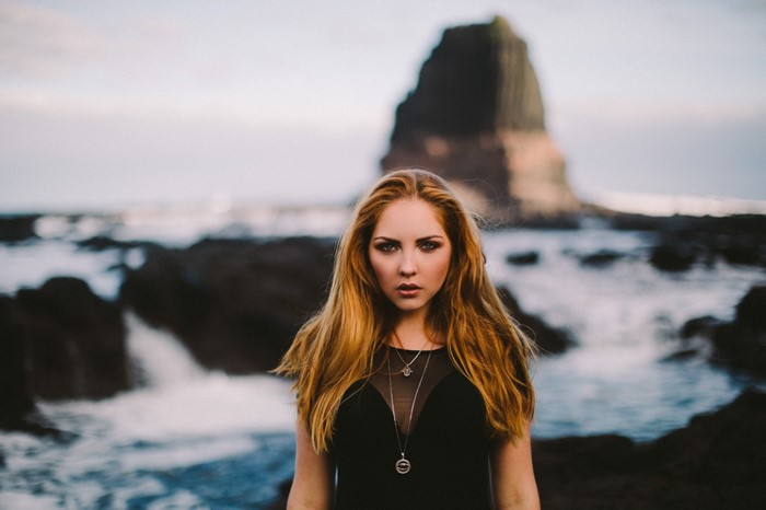 Woman in black dress on rocky beach with ocean background