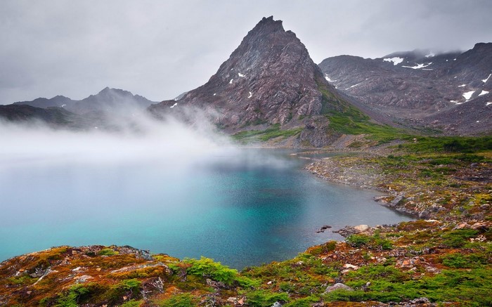 Misty mountain lake with rocky shores and green vegetation