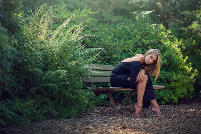 Woman in black dress sitting on a bench in a garden