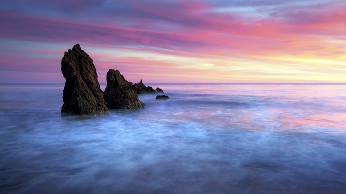 Rock formations in the ocean at sunset with colorful sky