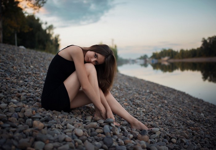 Woman in black dress sitting on a rocky shore by a river