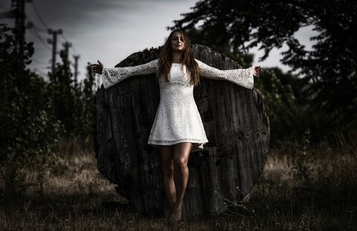 Woman in white dress standing by a wooden spool