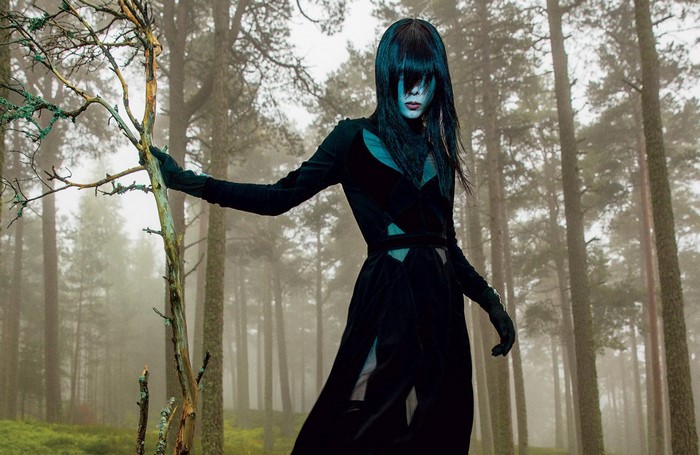 Woman in black costume in a foggy forest