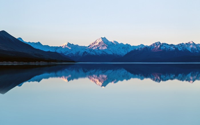 Snow-capped mountains reflected in a calm lake at dawn