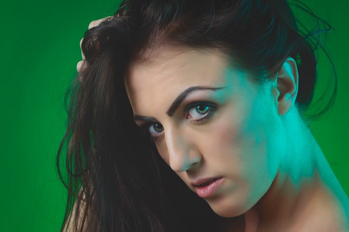Woman with dark hair and green eyes against a green background