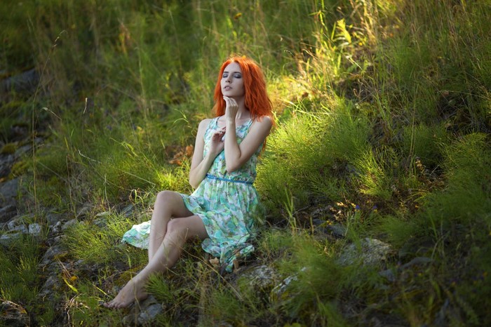 Redhead Woman Sitting in Sunlit Meadow