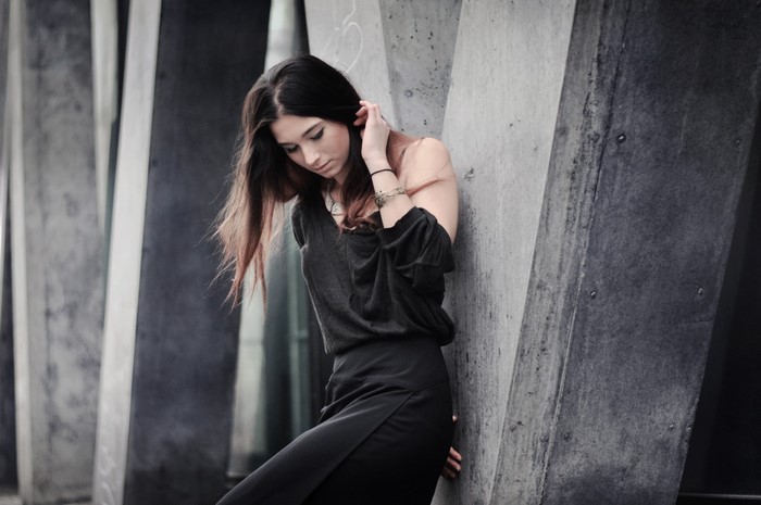 Woman in black dress leaning against concrete structure