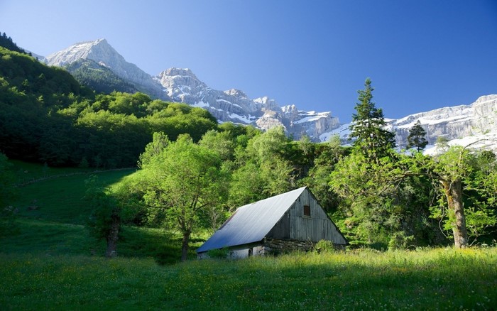 Wooden hut in a green mountain valley with snow-capped peaks