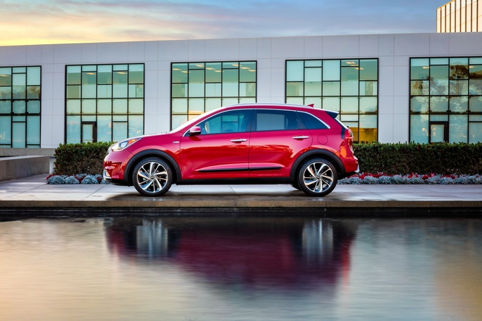 Red Kia Niro Crossover parked by a building with reflection
