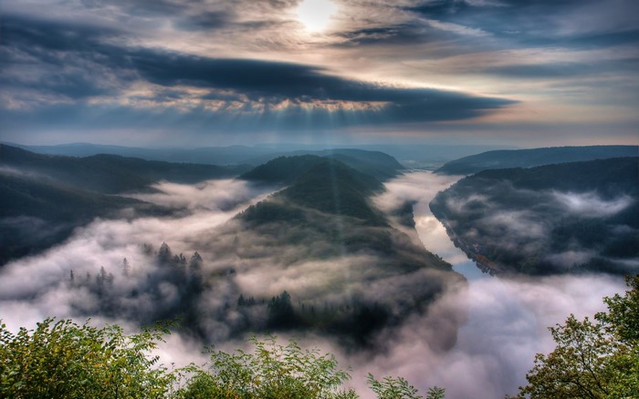 Misty river valley at sunrise with sunbeams