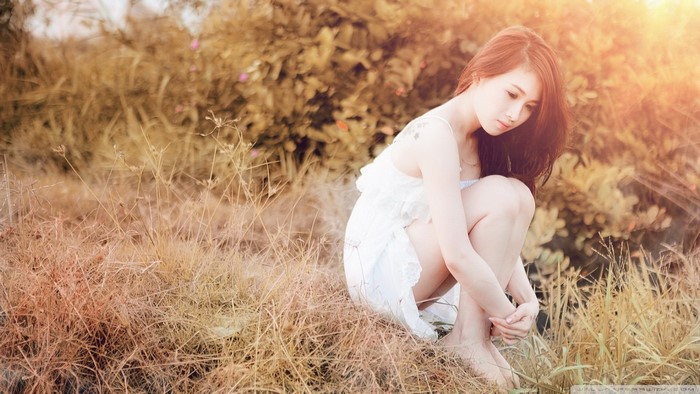 Woman in white dress sitting in dry grass