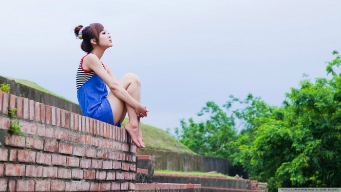 Young Woman Sitting on Brick Wall in Thoughtful Pose