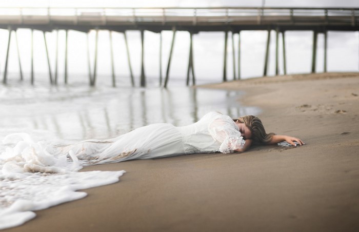 Woman in white dress lying on a beach near a pier
