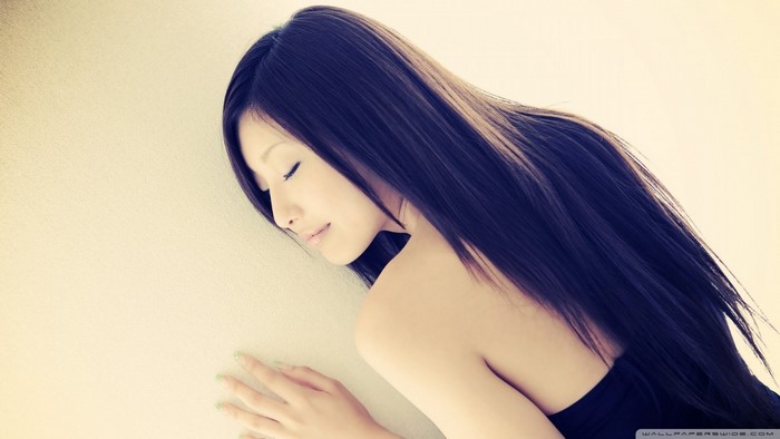 Woman with long black hair leaning against a wall