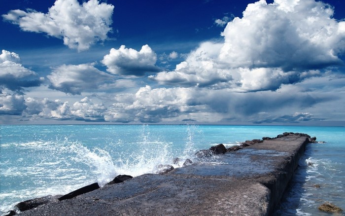 Concrete pier with waves crashing under a cloudy sky