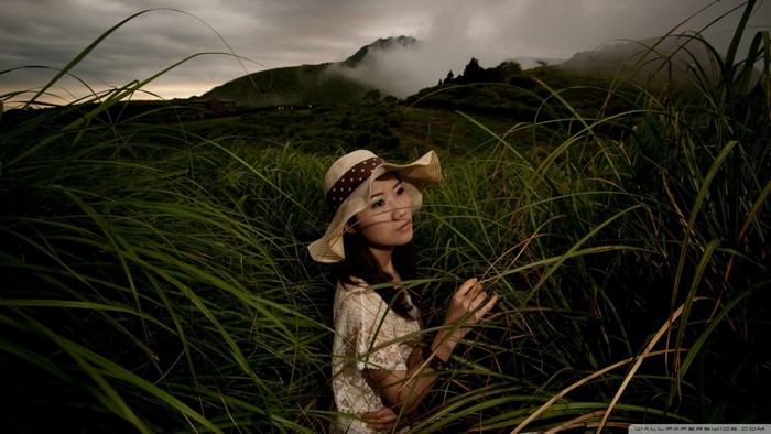 Woman in a hat in tall grass with mountains in the background