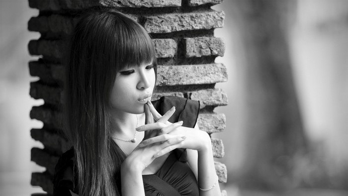 Monochrome portrait of a young Asian woman leaning against bricks