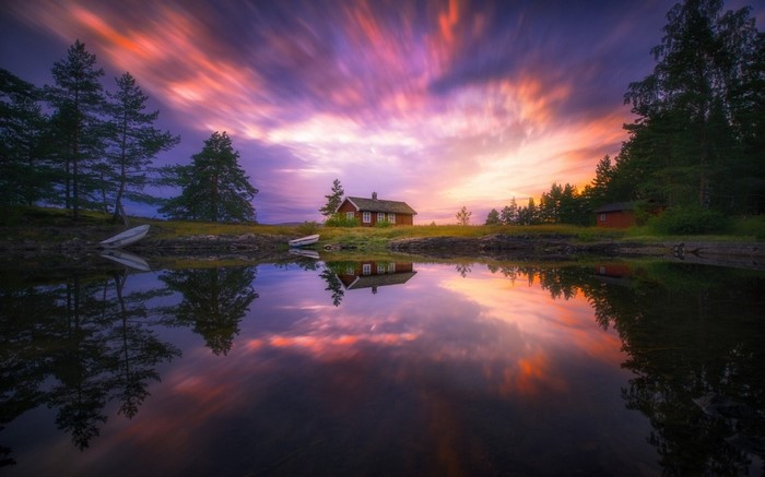 Red cottage by lake at sunset with colorful sky reflection