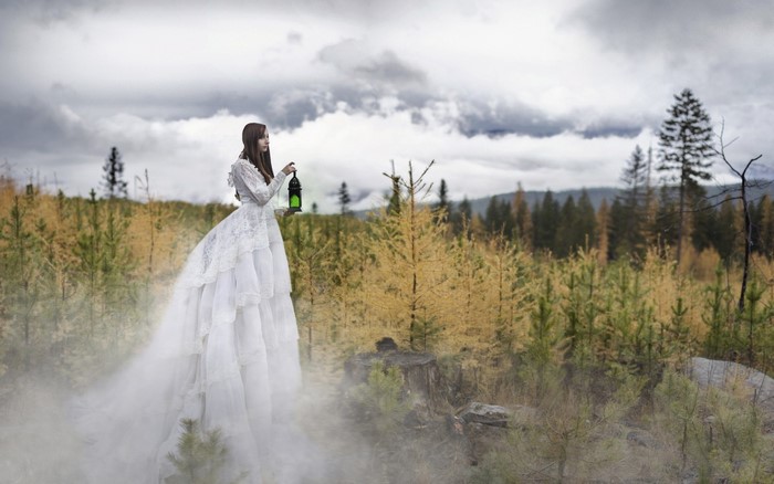 Woman in white dress holding a lantern in a misty forest
