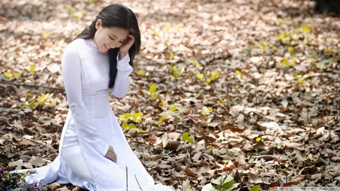 Woman in white dress sitting on fallen leaves