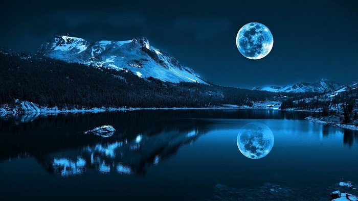 Full moon over a calm lake and mountains at night