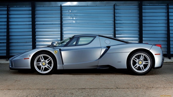 Silver Ferrari Enzo parked in front of a corrugated metal wall