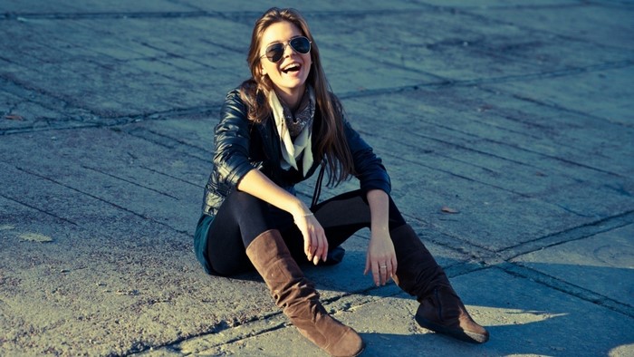 Woman wearing sunglasses and leather jacket sitting on pavement