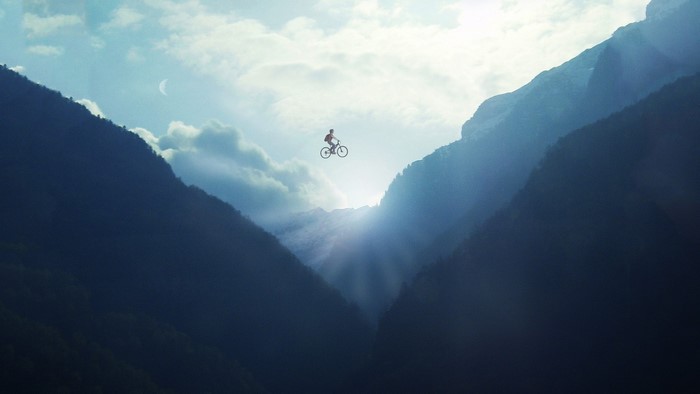 Cyclist jumping between mountains with sun rays