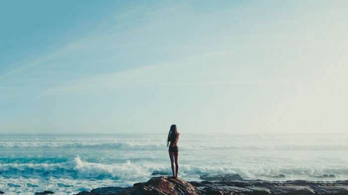 Woman standing on rocks by the ocean with waves