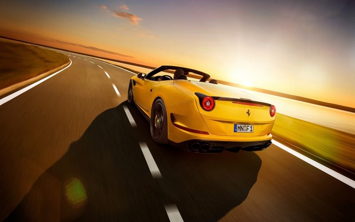 Yellow Ferrari California T driving on a road at sunset