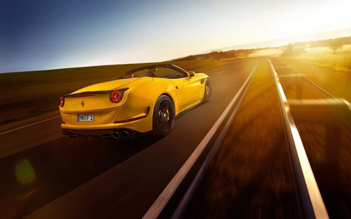 Yellow Ferrari California T driving on a road at sunset